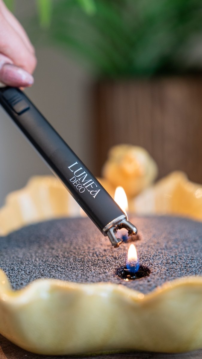 Allumage d'une bougie perlée noire à l'aide d'un briquet USB rechargeable Lumea Deco, dans un récipient coquillage jaune — accessoire pratique et élégant pour les amateurs de décoration.