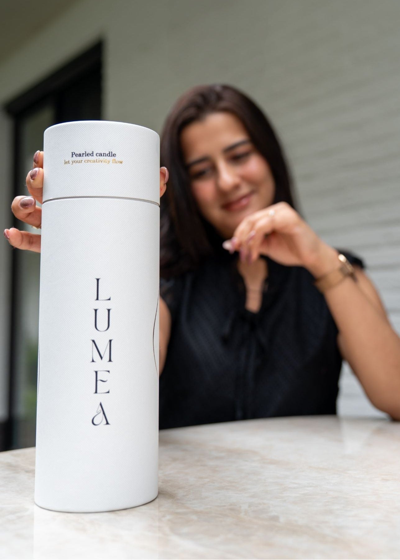 Femme présentant le packaging blanc de la bougie perlée Lumea, concept belge de bougie rechargeable, personnalisable et sans paraffine.