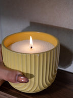 Bougie perlée allumée dans un pot en céramique jaune, tenue à la main, ambiance chaleureuse et moderne, parfaite pour offrir ou décorer son intérieur.