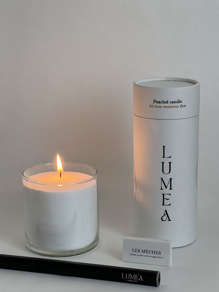 Bougie perlée allumée dans un verre transparent, accompagnée de son tube packaging Lumea Deco, d’un étui de mèches et d’un allume-bougie noir – solution décorative et rechargeable.