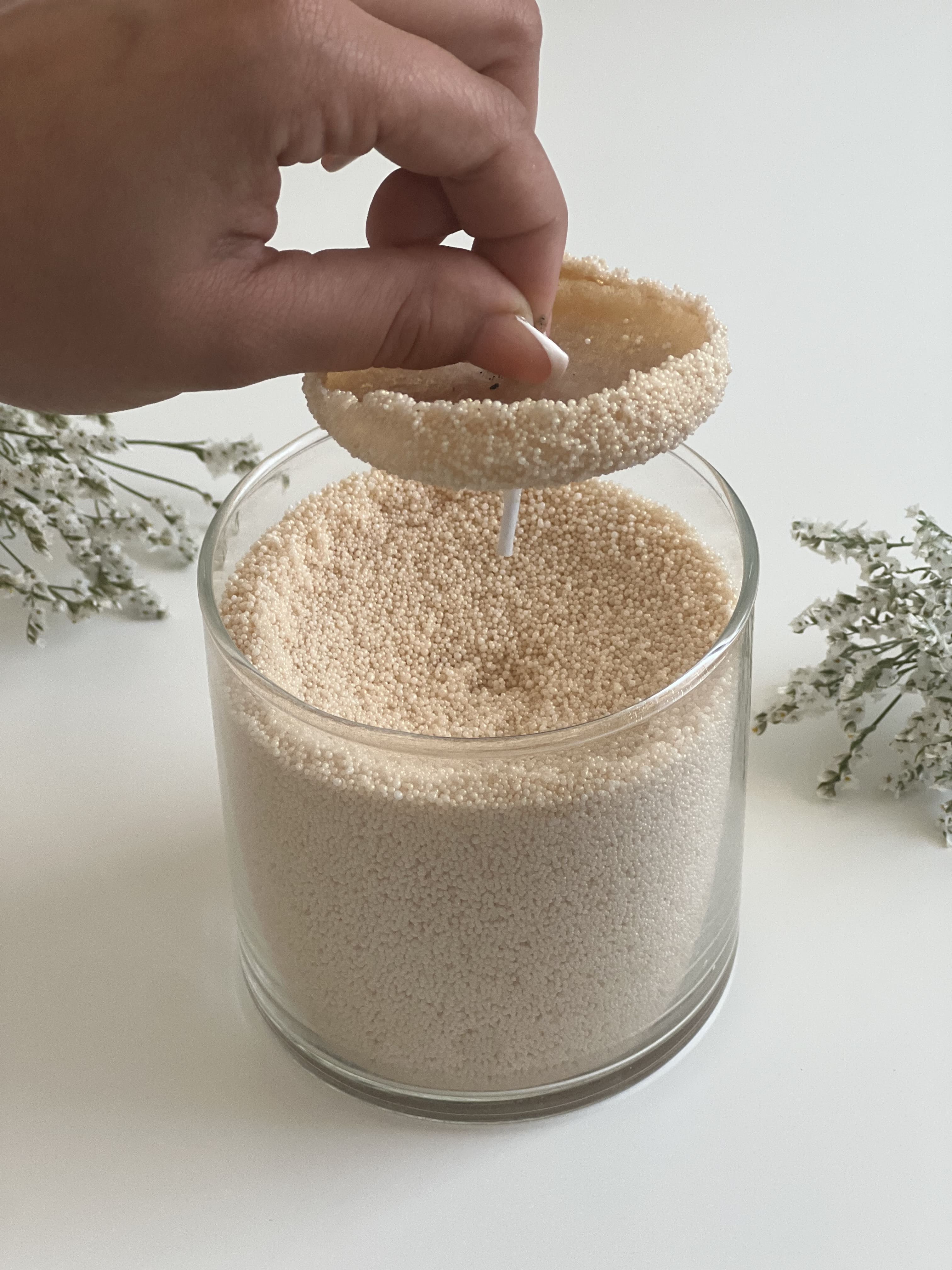 Retrait d’un bloc de cire consumée dans une bougie perlée blanche Lumea, illustrant la facilité de nettoyage et de recharge dans un contenant en verre.