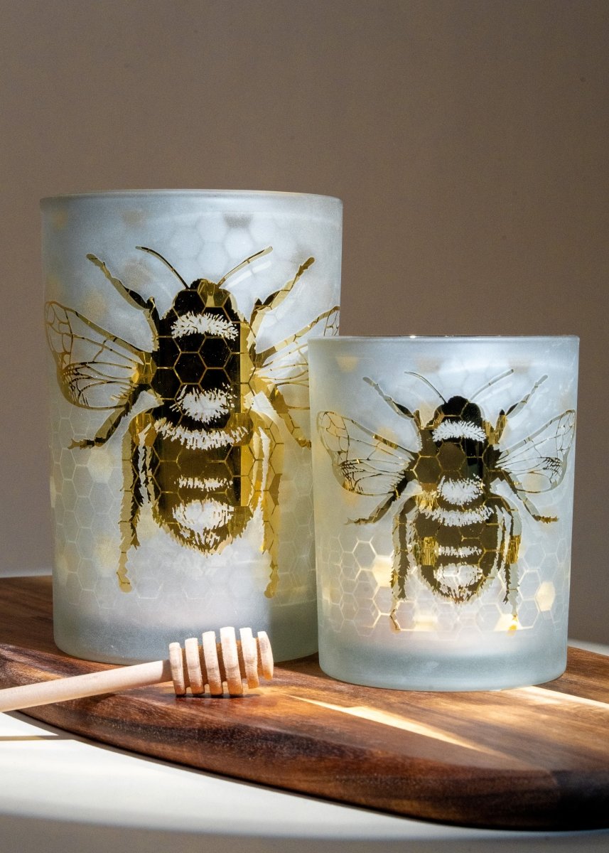 Duo de photophores en verre givré ornés d’un motif abeille dorée et alvéoles, effet lumineux chaleureux, posés sur planche en bois.