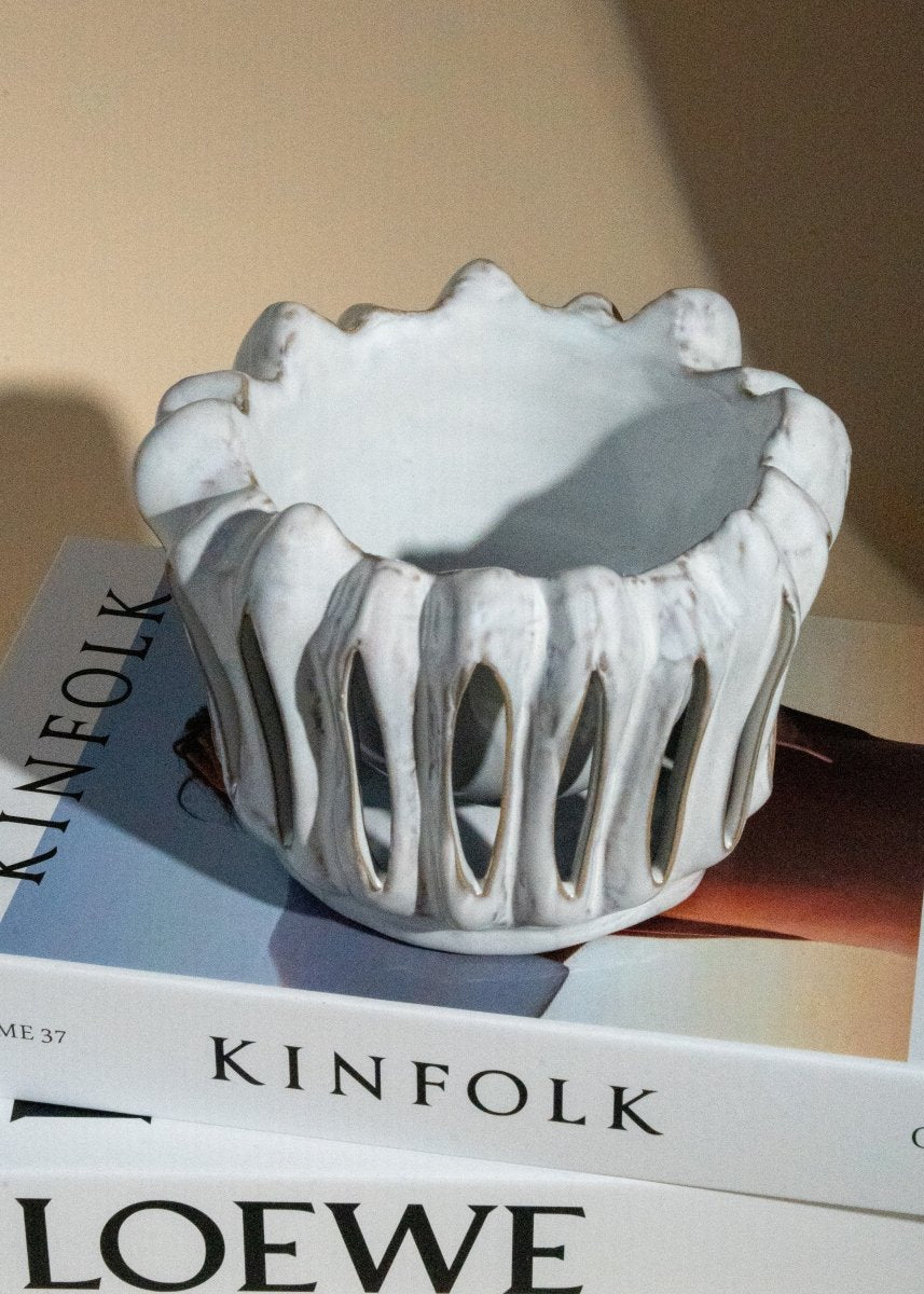Photophore en céramique blanche à structure ajourée et forme organique, posé sur des livres Kinfolk et Loewe dans une ambiance lumineuse naturelle.