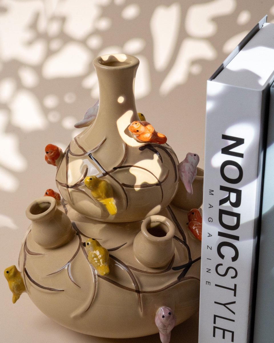 Vase en céramique beige à plusieurs colonnes orné de petits oiseaux colorés, placé à côté de livres de style nordique ; pièce originale parfaite pour une décoration d’intérieur chaleureuse ou comme idée cadeau déco.