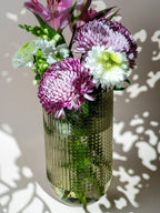 Vase en verre transparent à reliefs striés et en pois, contenant un bouquet de fleurs fraîches aux tons violets, blancs et roses – décoration florale raffinée, parfaite à offrir.