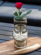 Vase en verre transparent rempli de galets blancs avec une rose rouge, décoration minimaliste et romantique, idéale pour un intérieur moderne ou une idée cadeau.
