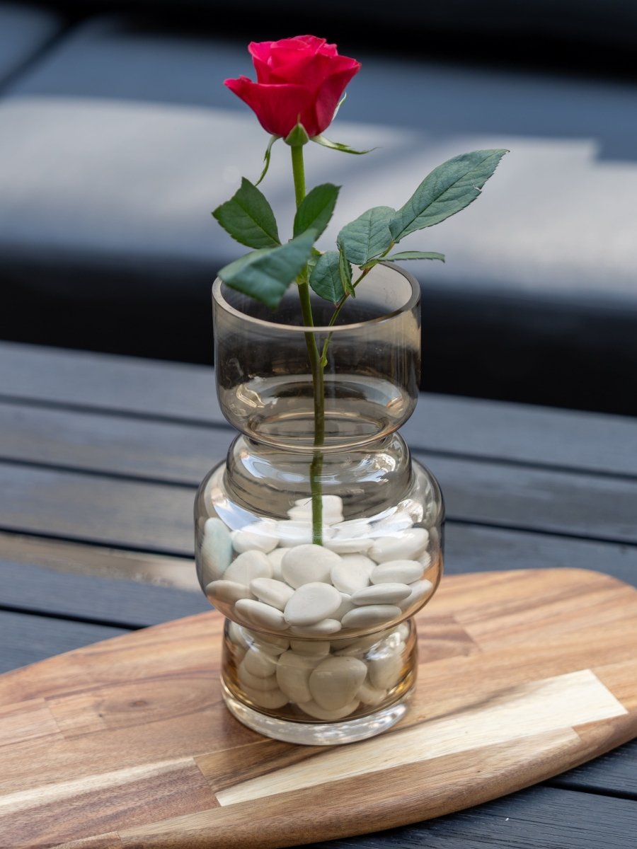 Vase en verre transparent rempli de galets blancs avec une rose rouge, décoration minimaliste et romantique, idéale pour un intérieur moderne ou une idée cadeau.