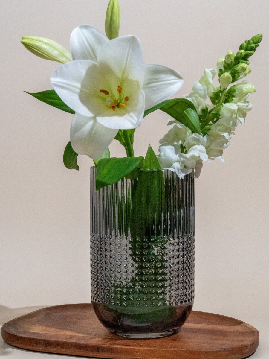 Vase en verre transparent à reliefs texturés avec motifs en pois et stries verticales, contenant un bouquet de fleurs blanches – idéal pour une décoration raffinée ou un cadeau élégant.